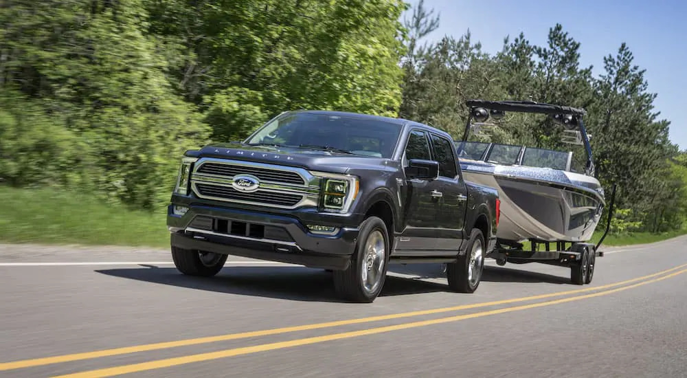 A dark grey 2022 Ford F-150 Limited towing a boat on the highway.