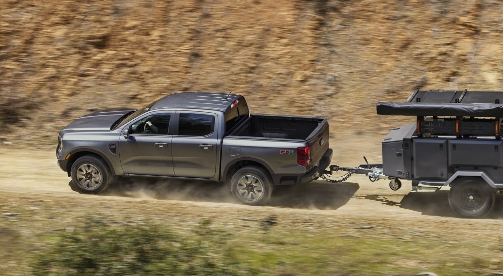 Side view of a grey 2025 Ford Ranger Raptor towing a small gear trailer.