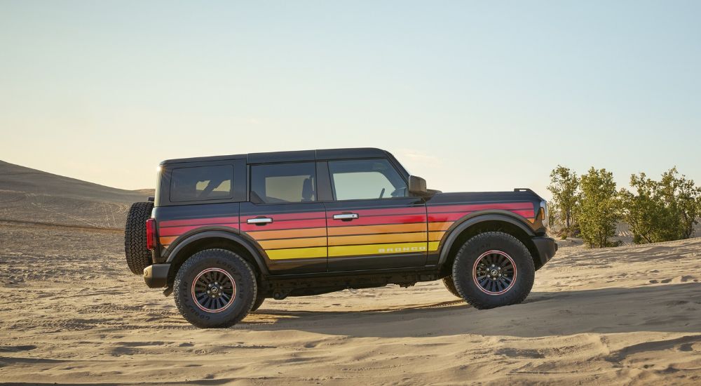 Side view of a multi-colored 2025 Ford Bronco Big Bend Free Wheeling driving on sand dunes.