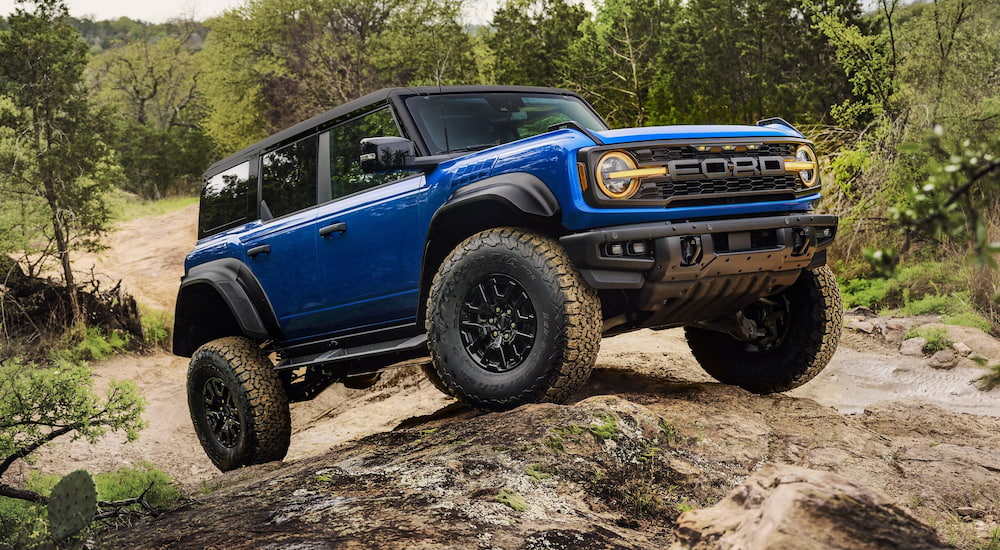A blue 2025 Ford Bronco Raptor off-roading on a rocky trail.