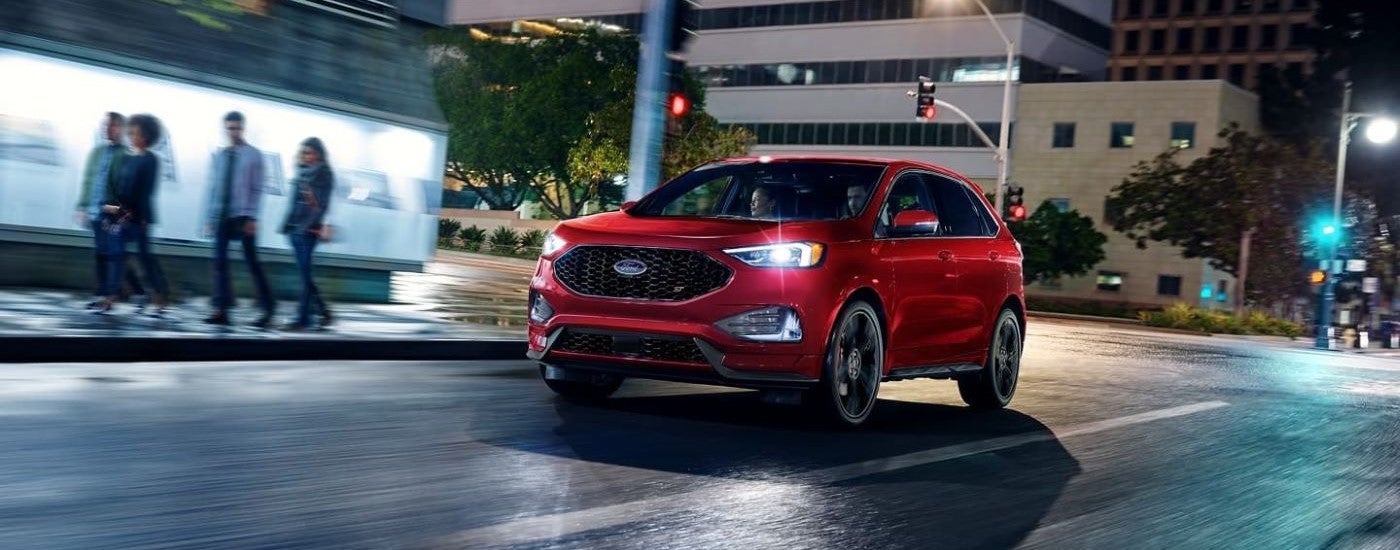 A red 2023 Ford Edge ST driving through a city intersection.