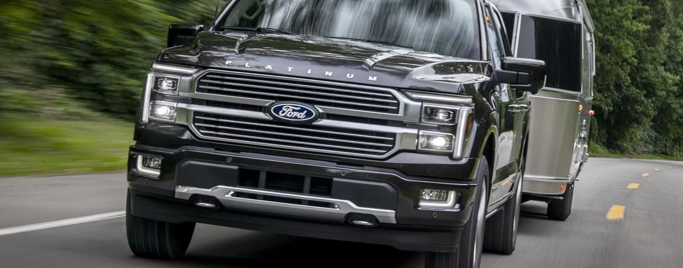 A close up of a black 2024 Ford F-150 Platinum Hybrid towing a silver camper.